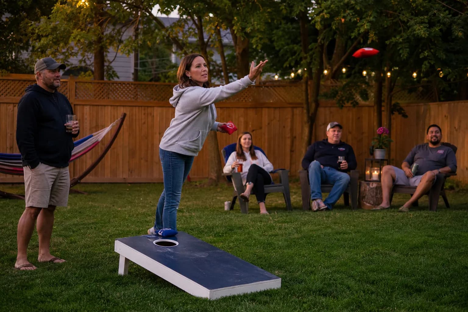 Friends playing cornhole in a backyard on a summer evening